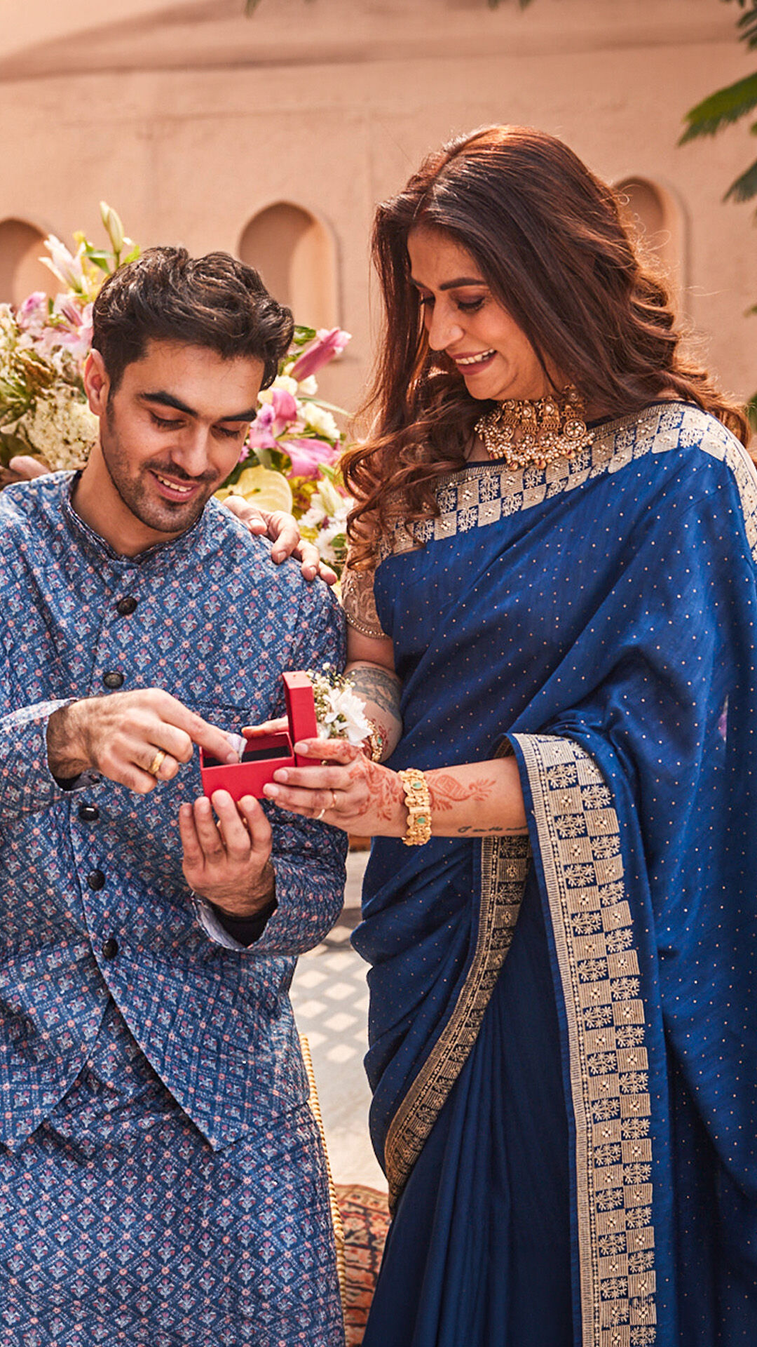 Mother and son in blue ethnic wear sharing a warm Mother&rsquo;s Day moment in a festive floral setting.
